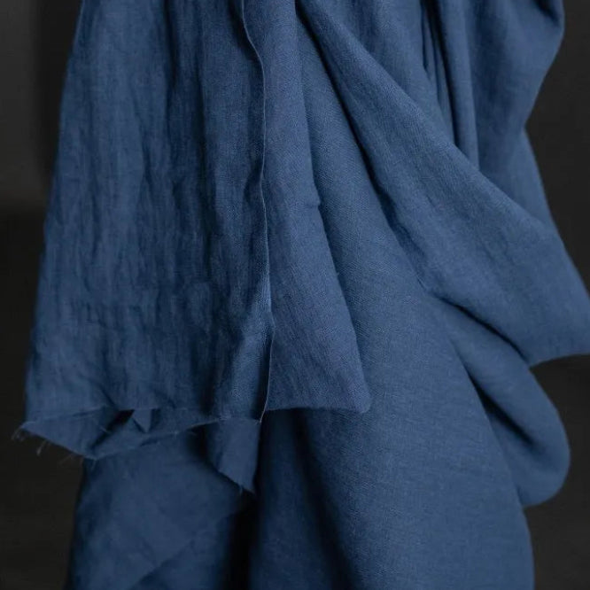 185 European Linen in Goodnight by Merchant and Mills. Available at Stitch Piece Loop – Australian Fabric Store. The image is a close up of the dark blue fabric draped over the fabric roll against a dark background.