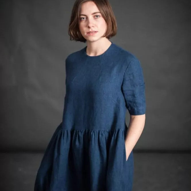 185 European Linen in Goodnight by Merchant and Mills. Available at Stitch Piece Loop – Australian Fabric Store. The image is a woman wearing the Ellis Dress made up in the Goodnight linen against a dark background.