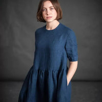 185 European Linen in Goodnight by Merchant and Mills. Available at Stitch Piece Loop – Australian Fabric Store. The image is a woman wearing the Ellis Dress made up in the Goodnight linen against a dark background.