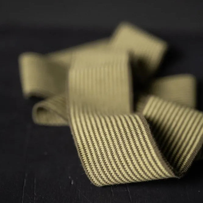Club Camo Cotton Ribbing. A playful mustard and khaki striped rib trim. The image is a pre-cut length of the rib trim against a dark background.