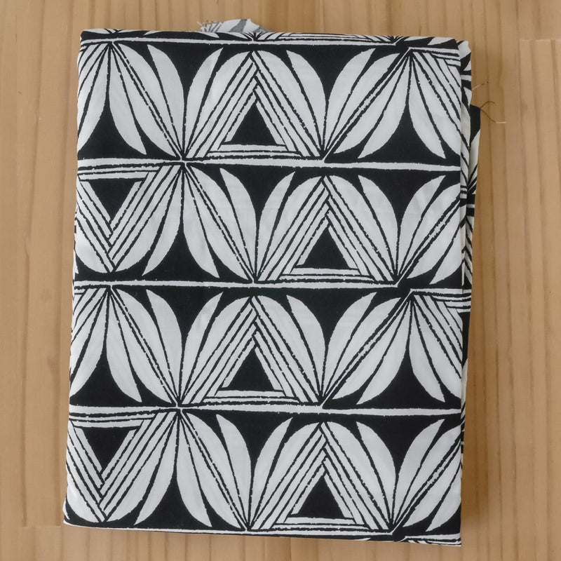 A folded piece of fabric with a black and white geometric pattern of repeating leaf and triangle motifs, lying flat on a light wood grain surface.