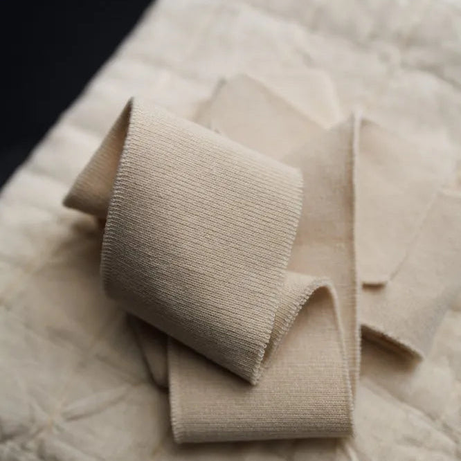 Ecru cotton ribbing by Merchant and Mills available at Stitch Piece Loop – Australian Fabric Store. The image is a close up of the ribbing sitting on a natural quilted cotton against a dark background.