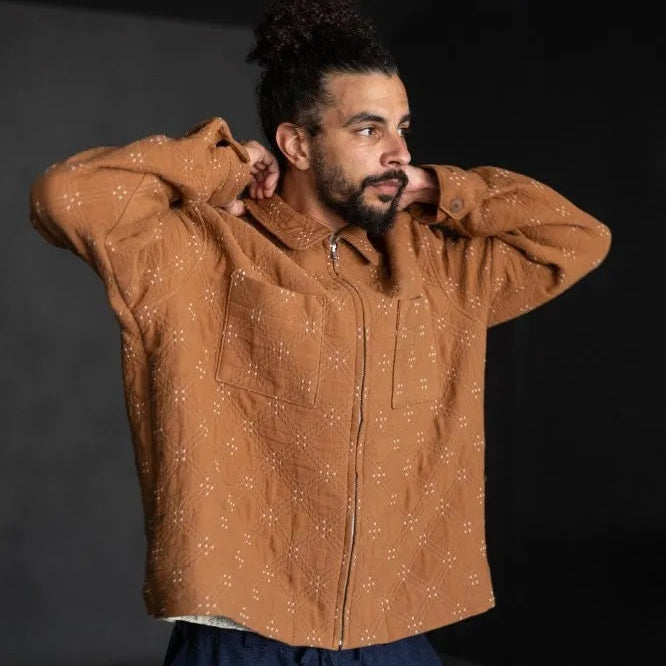 Goldie quilted cotton jacquard fabric in ochre and cream, reversible double-cloth texture, with cream embroidered details. The fabric has been made up into a jacket with the image showcasing the garment on a man with the front closed.