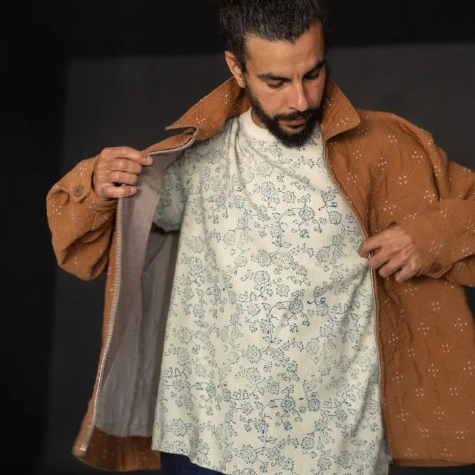 Goldie quilted cotton jacquard fabric in ochre and cream, reversible double-cloth texture, with cream embroidered details. The fabric has been made up into a jacket with the image showcasing the garment on a man with the front open.