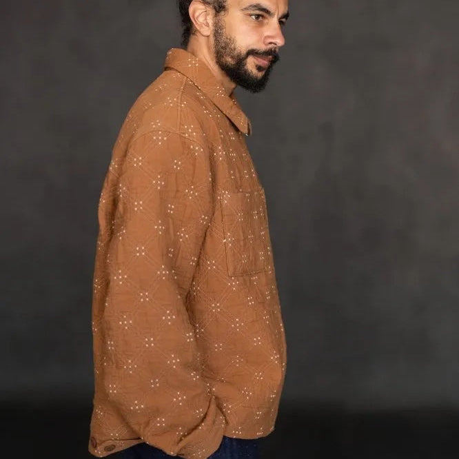 Goldie quilted cotton jacquard fabric in ochre and cream, reversible double-cloth texture, with cream embroidered details. The fabric has been made up into a jacket with the image showcasing the garment on a man from a side view.