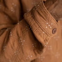 Goldie quilted cotton jacquard fabric in ochre and cream, reversible double-cloth texture, with cream embroidered details. The fabric has been made up into a jacket with the image showcasing the sleeve and cuff details.