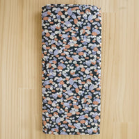 Folded fabric end of bolt remnant, featuring a dense multicolor terrazzo pattern on a black background, laid flat on a light wood surface.