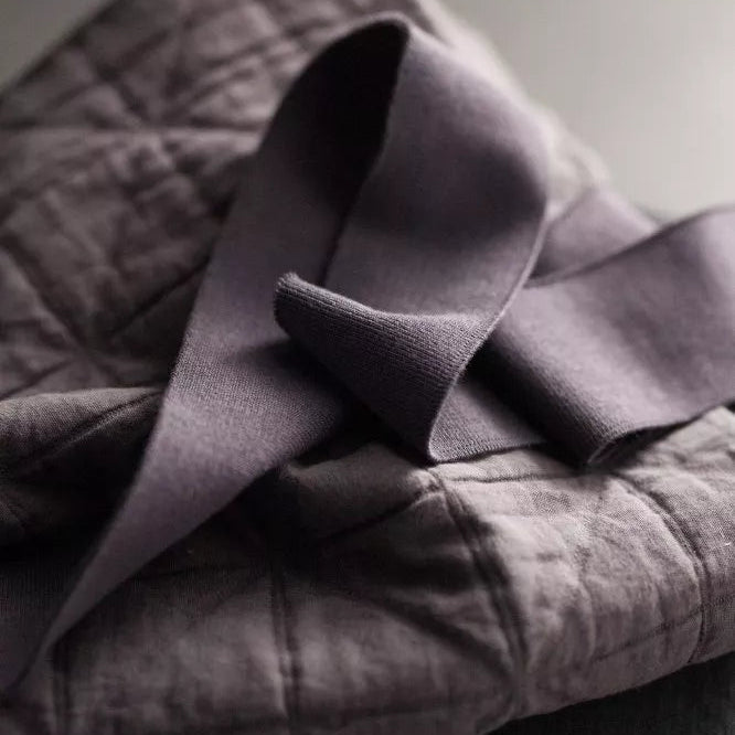 Mauve Grey Cotton Ribbing by Merchant and Mills, available at Stitch Piece Loop – Australian Fabric Store. This image is a close up of the ribbing sitting on a grey quilted cotton against a dark background.