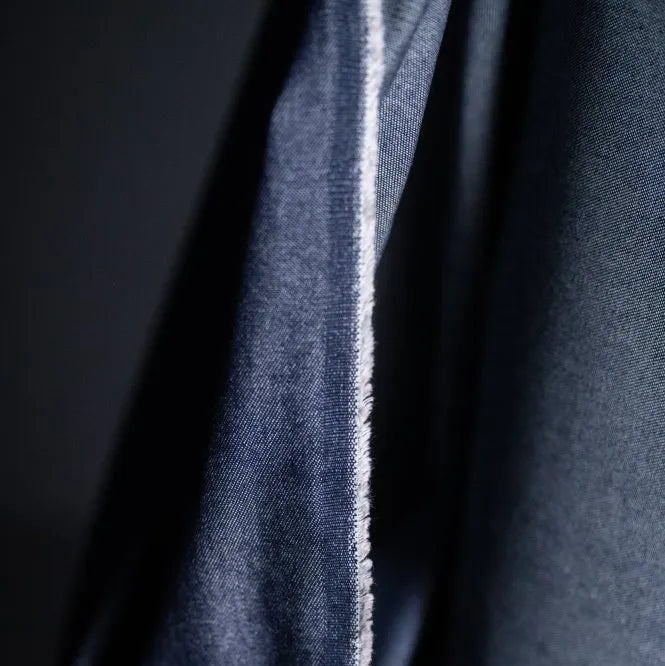 Merchant and Mills 8oz Washed Denim in Dark. The fabric is draped over the roll and the image is a close up of the selvedge.