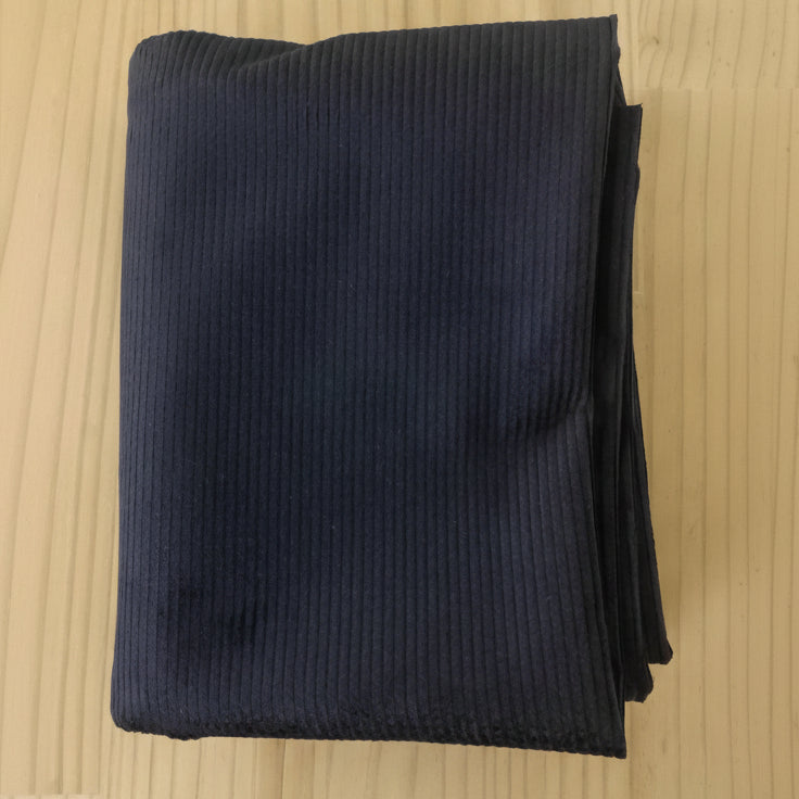 A folded navy 8 wale corduroy in navy, displayed on a light wood grain surface.