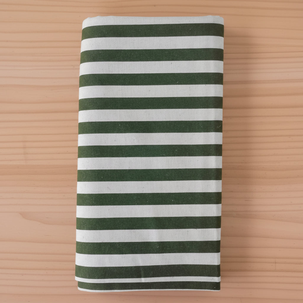 Folded cotton canvas fabric item, featuring horizontal stripes in dark forest green and light green, laid flat on a light wood grain surface.