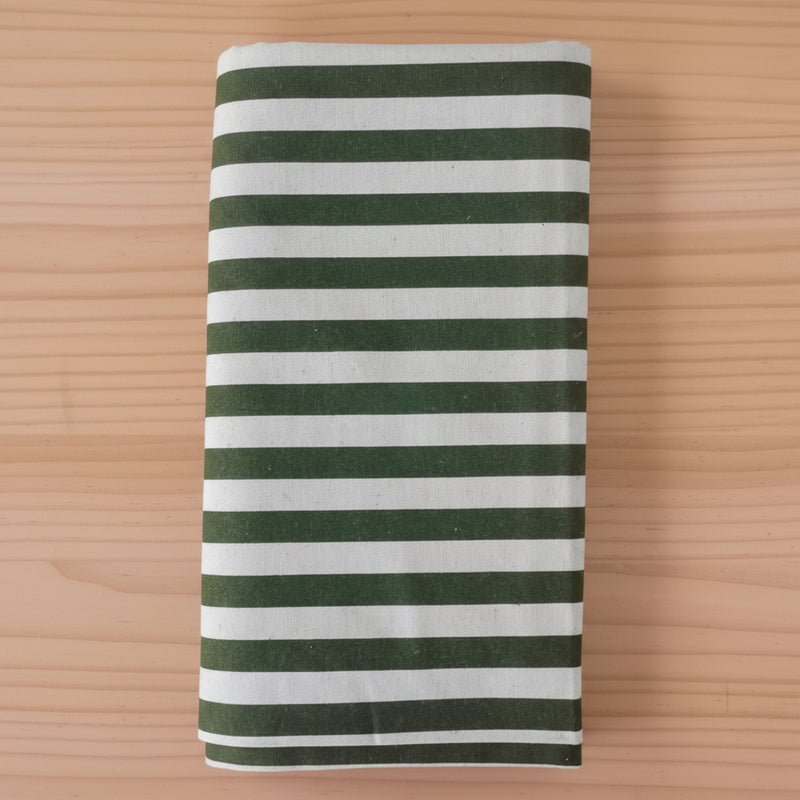 Folded cotton canvas fabric item, featuring horizontal stripes in dark forest green and light green, laid flat on a light wood grain surface.