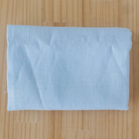 A folded light blue linen fabric piece, laid flat on a light-colored wooden surface.