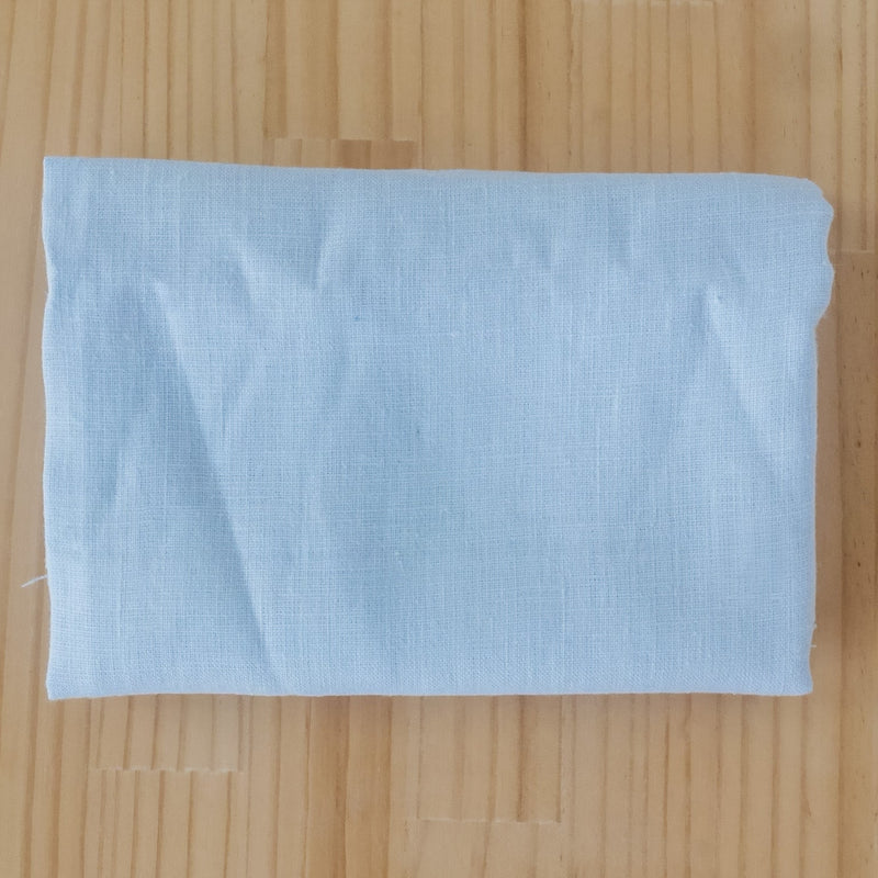 A folded light blue linen fabric piece, laid flat on a light-colored wooden surface.