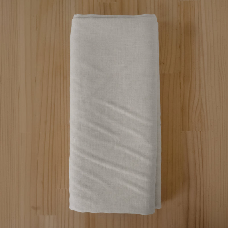 A folded piece of light beige or off-white linen fabric, laid flat on a light brown wooden surface.