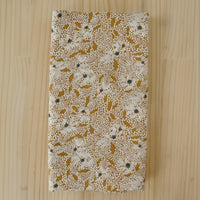 A folded length of viscose crepe fabric with an abstract floral print in white, mustard and pale pink on a light wooden background.