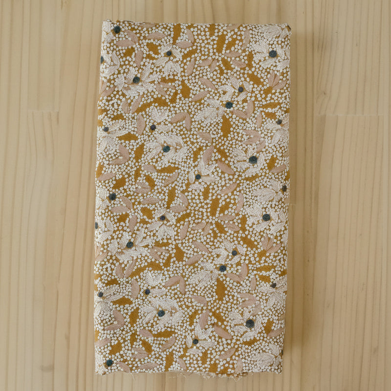 A folded length of viscose crepe fabric with an abstract floral print in white, mustard and pale pink on a light wooden background.