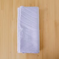 A folded piece of light lavender linen fabric, displayed on a light wood grain surface.