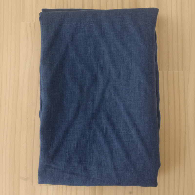 A folded piece of dark blue linen fabric laid flat on a light-colored wooden surface.