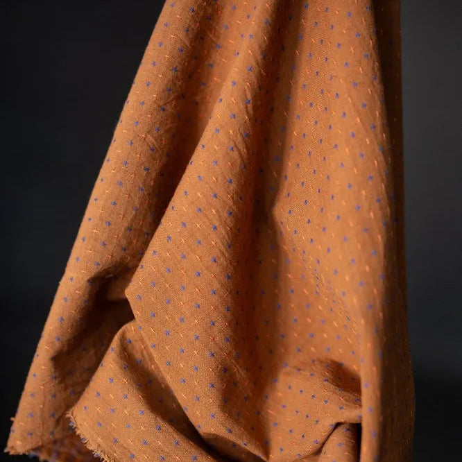 Rust Bobbette Organic Indian Cotton with Orange and Cobalt Blue woven Cross Stitch Detail. A photo of the draped fabric on the roll.