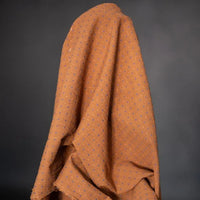 Rust Bobbette Organic Indian Cotton with Orange and Cobalt Blue woven Cross Stitch Detail. A photo of the fabric draped over the roll.