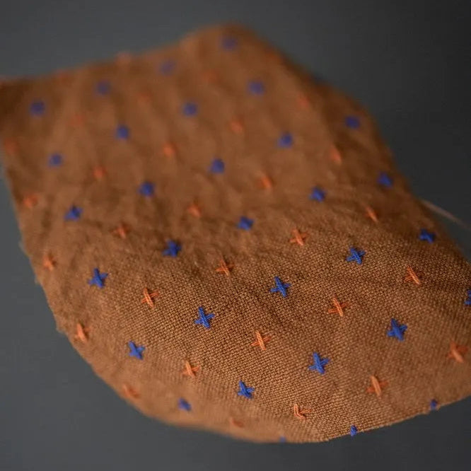 Rust Bobbette Organic Indian Cotton with Orange and Cobalt Blue woven Cross Stitch Detail. A close up of a fabric swatch.
