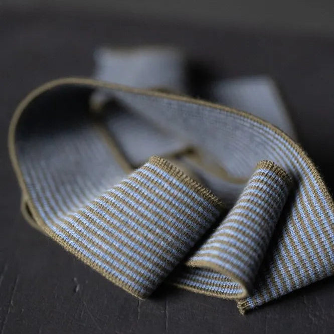 Sierra sea cotton rib trim by Merchant and Mills. A khaki green and denim blue striped rib trim, perfect for necklines and cuffs on tees and sweatshirts. The image shows a close up of the trim on a dark background.