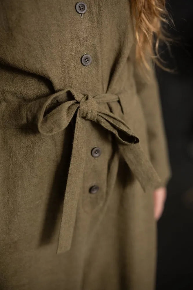 Close-up of a person wearing a long sleeved, green cassidy jumpsuit on a dark background