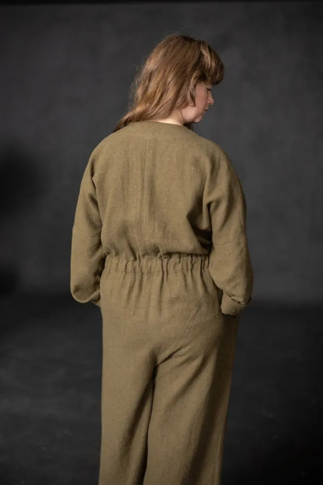 The back view of a person wearing a long sleeved greem cassidy jumpsuit against a dark background
