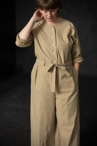Woman wearing a beige cassidy jumpsuit against a dark background