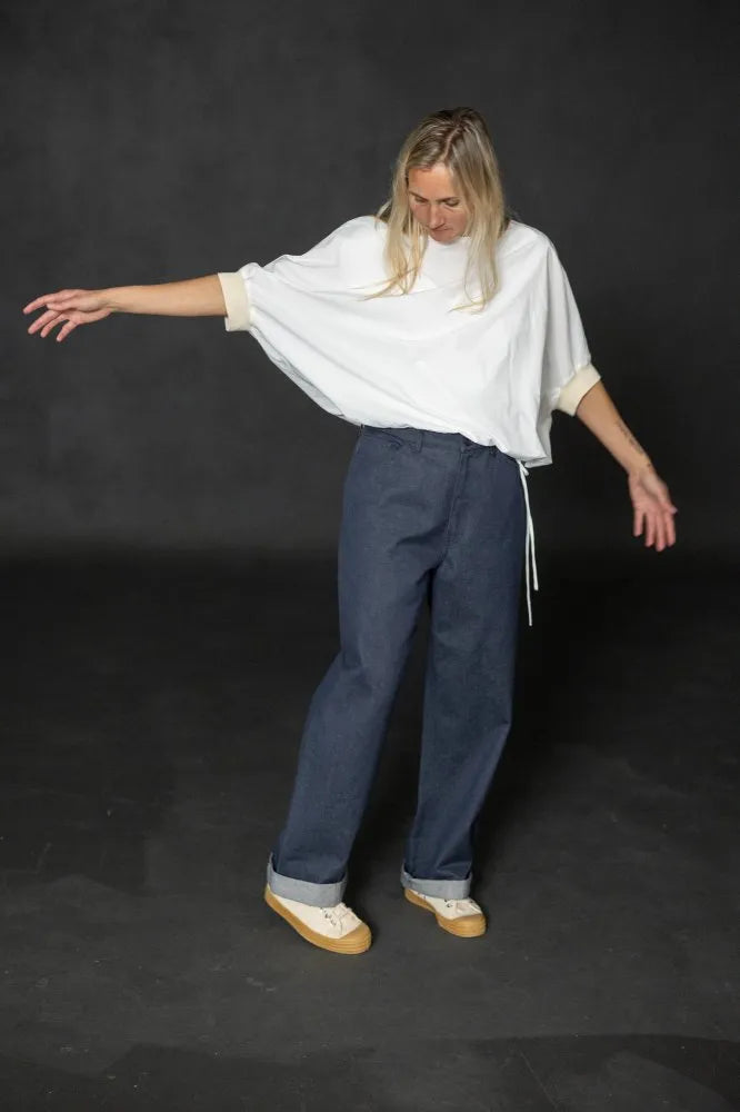 Person wearing a white cirrus top and blue pants on a black background. The Cirrus Top sewing pattern by Merchant and Mills is available at Stitch Piece Loop, Australia.