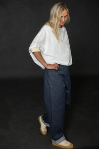 Person wearing a white cirrus top and blue pants on a black background. The Cirrus Top sewing pattern by Merchant and Mills is available at Stitch Piece Loop, Australia.
