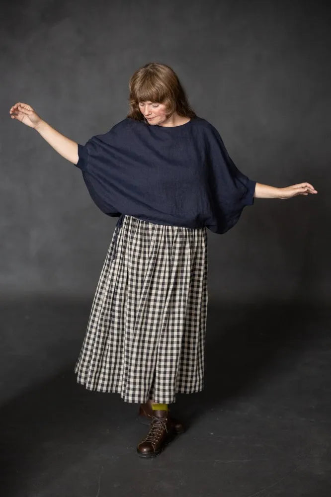 Person wearing a dark navy cirrus top and checked skirt on a black background. The Cirrus Top sewing pattern by Merchant and Mills is available at Stitch Piece Loop, Australia.