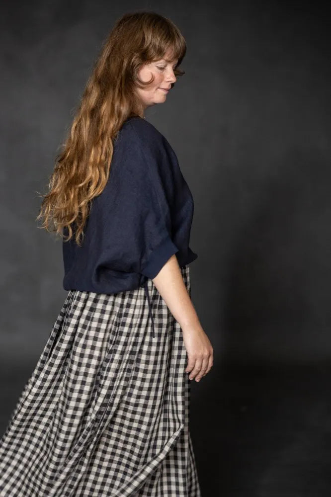 Person wearing a dark navy cirrus top and checked skirt on a black background. The Cirrus Top sewing pattern by Merchant and Mills is available at Stitch Piece Loop, Australia.