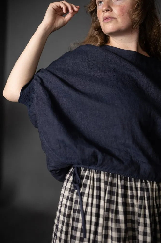 Person wearing a dark navy cirrus top and checked skirt on a black background. The Cirrus Top sewing pattern by Merchant and Mills is available at Stitch Piece Loop, Australia.