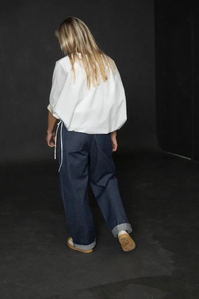 Person wearing a white cirrus top and blue pants on a black background. The Cirrus Top sewing pattern by Merchant and Mills is available at Stitch Piece Loop, Australia.