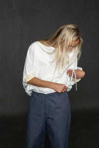 Person wearing a white cirrus top and blue pants on a black background, showcasing the drawstring detail. The Cirrus Top sewing pattern by Merchant and Mills is available at Stitch Piece Loop, Australia.