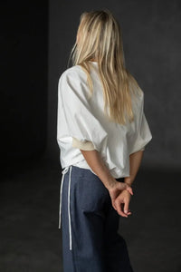 Person wearing a white cirrus top and blue pants on a black background. The Cirrus Top sewing pattern by Merchant and Mills is available at Stitch Piece Loop, Australia.