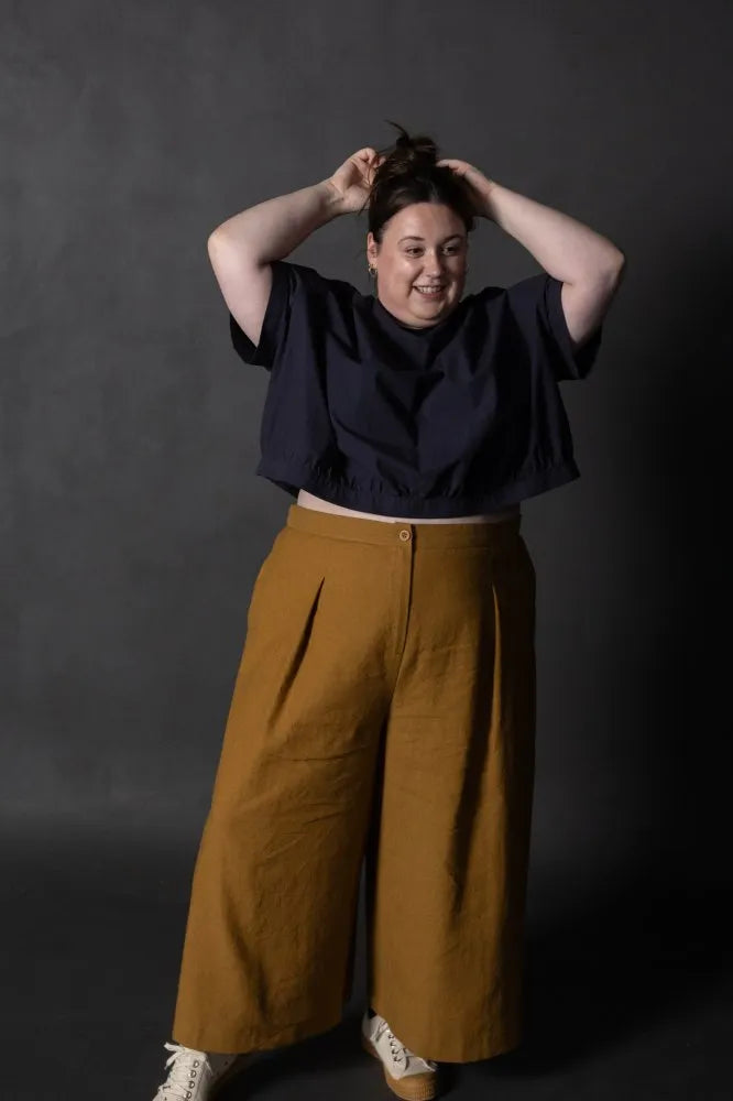 Person wearing a mustard yellow pair of Juno Trousers against a dark background. The Juno Trouser sewing pattern is by Merchant and Mills, and available at Stitch Piece Loop, Australia.