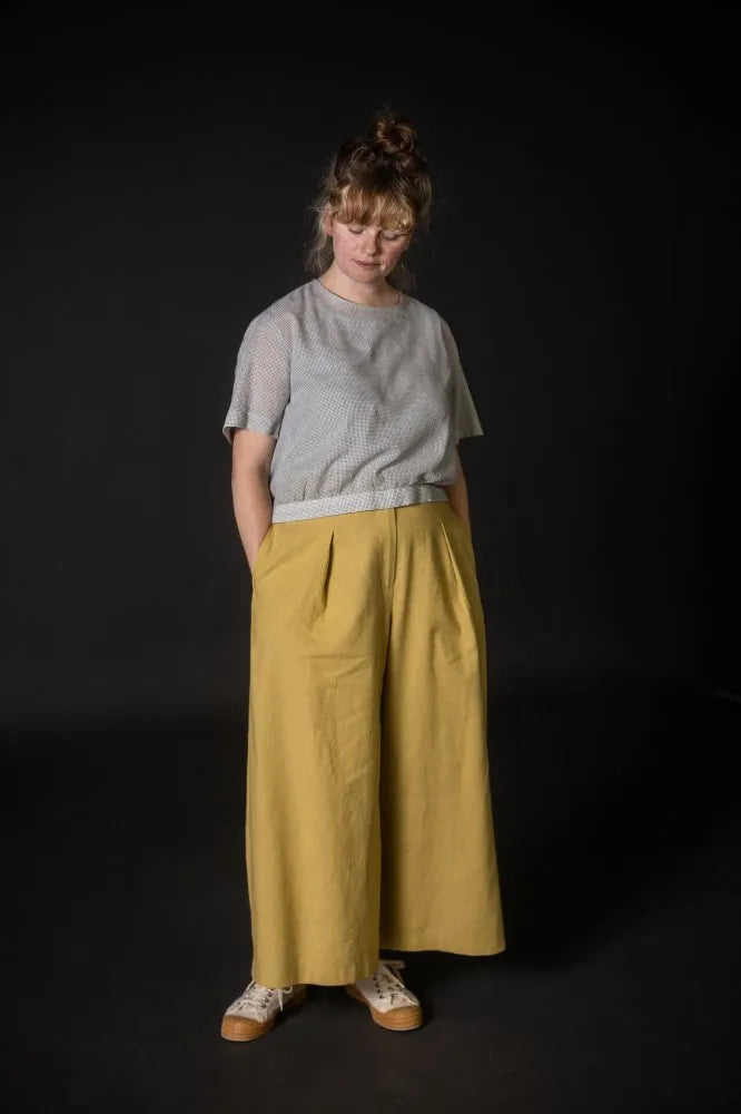 Person wearing a yellow pair of Juno Trousers against a dark background. The Juno Trouser sewing pattern is by Merchant and Mills, and available at Stitch Piece Loop, Australia.