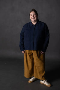 Person wearing a mustard yellow pair of Juno Trousers against a dark background. The Juno Trouser sewing pattern is by Merchant and Mills, and available at Stitch Piece Loop, Australia.