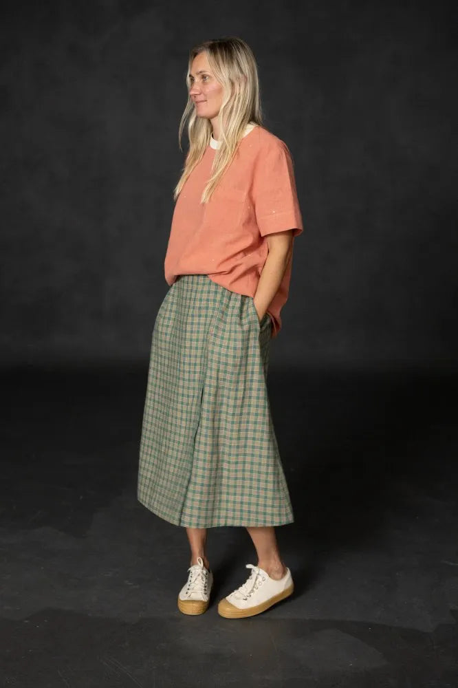 Woman wearing a green plaid Nevis skirt with a coral tee and white sneakers. The Nevis Skirt Sewing Pattern is designed by Merchant and Mills and available at Stitch Piece Loop Australia.