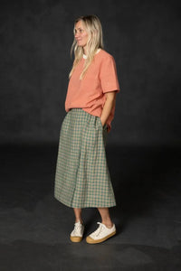 Woman wearing a green plaid Nevis skirt with a coral tee and white sneakers. The Nevis Skirt Sewing Pattern is designed by Merchant and Mills and available at Stitch Piece Loop Australia.