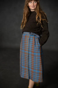 Woman wearing a blue plaid Nevis skirt with a dark brown knit top and boots. The Nevis Skirt Sewing Pattern is designed by Merchant and Mills and available at Stitch Piece Loop Australia.