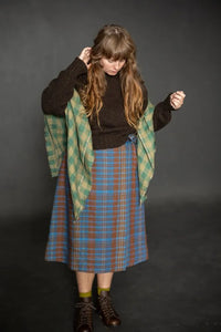 Woman wearing a blue plaid Nevis skirt with a dark brown knit top and boots. The Nevis Skirt Sewing Pattern is designed by Merchant and Mills and available at Stitch Piece Loop Australia.