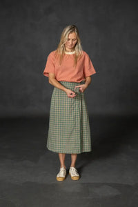 Woman wearing a green plaid Nevis skirt with a coral tee and white sneakers. The Nevis Skirt Sewing Pattern is designed by Merchant and Mills and available at Stitch Piece Loop Australia.