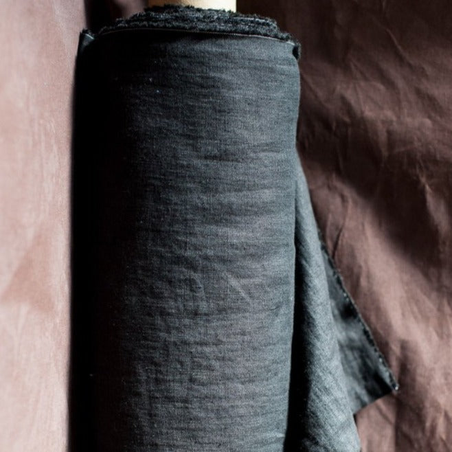 Merchant and Mills European Laundered Linen 185 in Scuttle Black Australia Stitch Piece Loop. Image is of the fabric on a roll with a dark brown background.