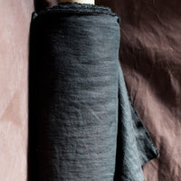 Merchant and Mills European Laundered Linen 185 in Scuttle Black Australia Stitch Piece Loop. Image is of the fabric on a roll with a dark brown background.